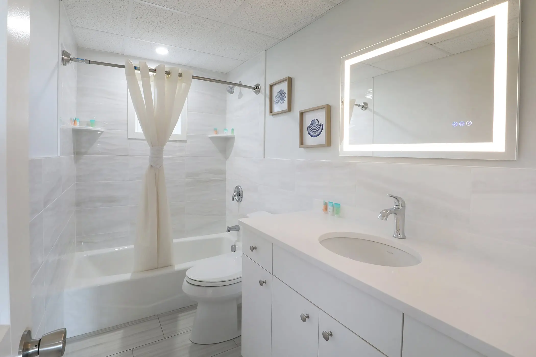 One of the two full bathrooms in a Type 8 Two-Bedroom Unit at the Matador, with a tub and shower, white vanity and lit mirror