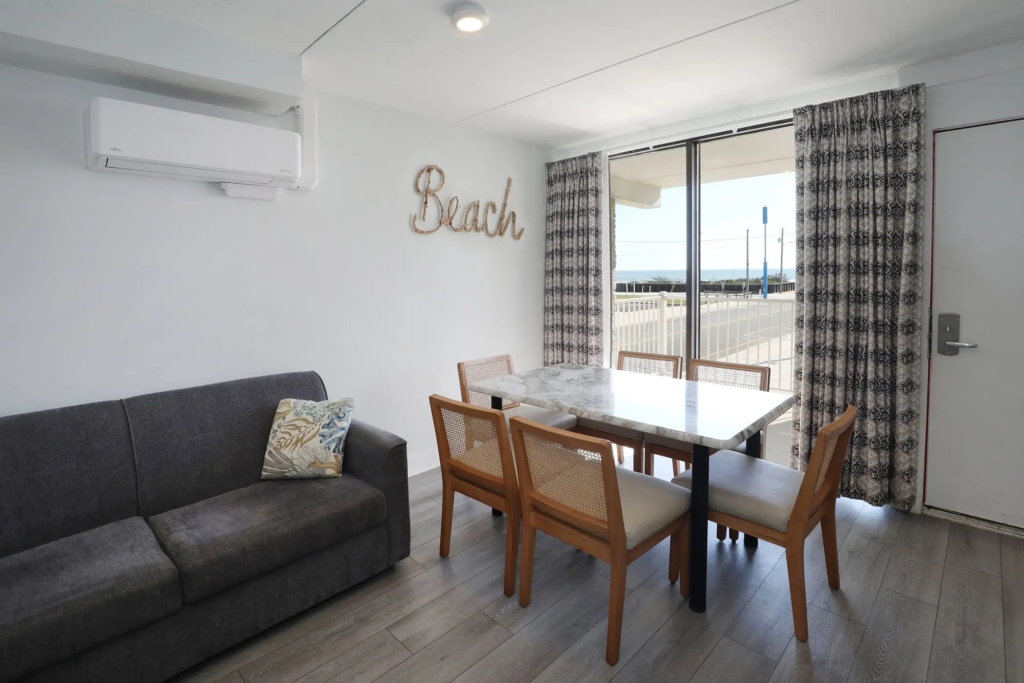 The living area of a Type 8 Two-Bedroom Unit at the Matador: a grey sofa bed and a dining table for six by the sliding glass door